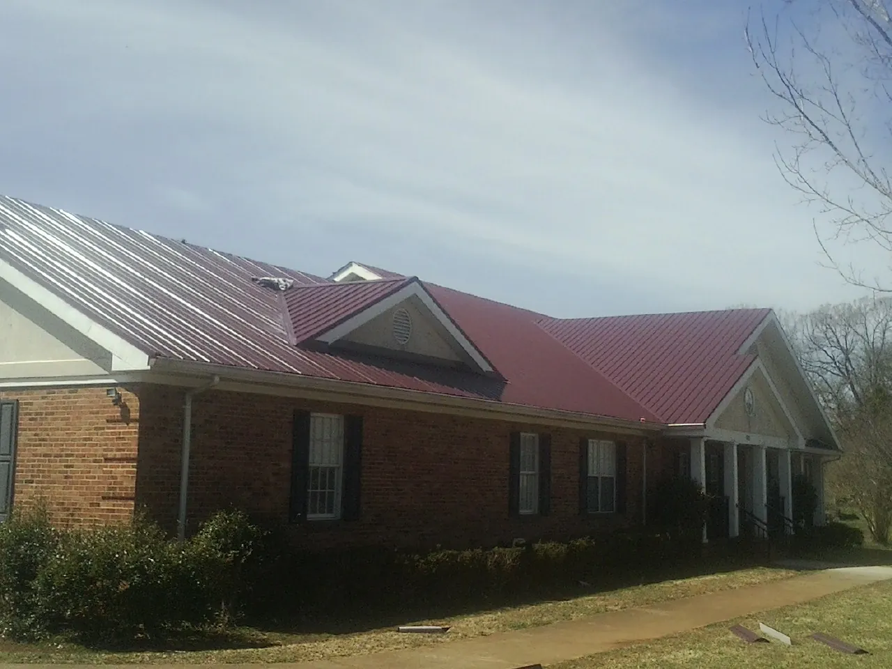 Red metal roof with gabled entries on a long brick building, from a Hail Damage Roof Repair job in Chatsworth